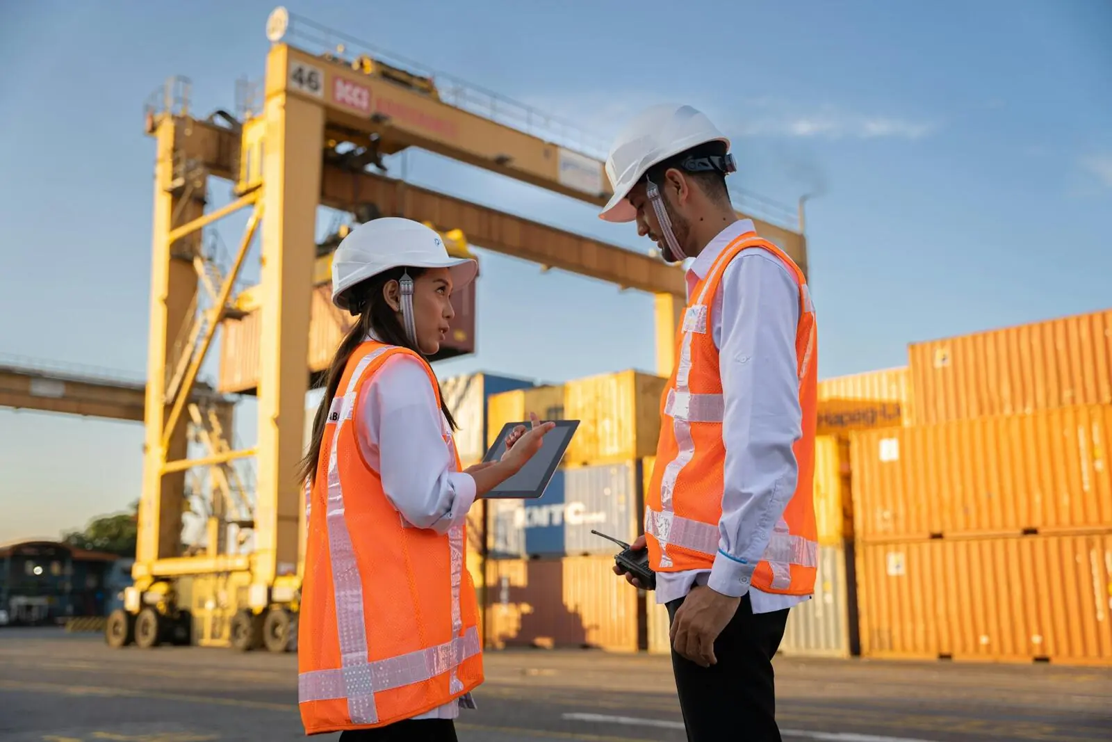 Two workers in hard hats reviewing plans beside shipping containers